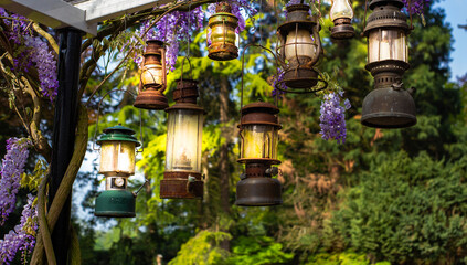 glowing Romantic candle lanterns hanging in garden vintage lamps in nature, stylish antique decoration with colorful flowers