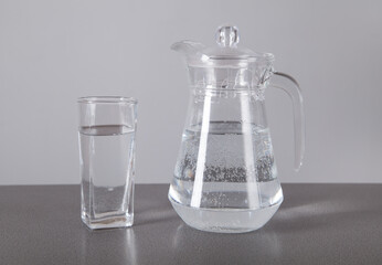 Glass and jug with of water, on  gray background.