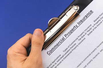 Man hold commercial property insurance claim form and policy in hand. Company real estate contract...