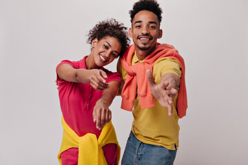 Obraz premium Brunette guy and woman in colorful T-shirts reach for camera. Pretty girl in red shirt and man in yellow tee smile on isolated backdrop