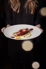 Female holding plate with baked duck breast with beetroot, daikon and bechamel