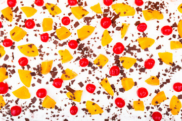 Creamy layered cake with chocolate, cherry and peach pieces on top, top view.