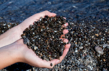 stones in the hands of the boy in the form of a heart on the background of the sea
