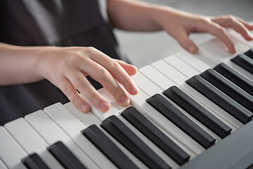 Fototapeta premium Hobby concept. A girl in a gray dress plays an electronic piano. Morning lifht on window. Close up