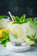 Two glass with lemonade or mojito cocktail with lemon and mint, cold refreshing drink or beverage with ice on rustic blue background