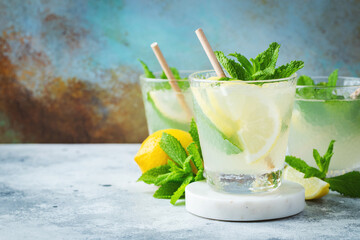 Two glass with lemonade or mojito cocktail with lemon and mint, cold refreshing drink or beverage with ice on rustic blue background. Copy space