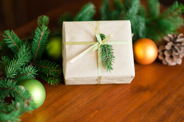Christmas gift box with Christmas tree branch decor and gold ribbon on a wooden brown background. Christmas balls and cones. copy space. Recycled paper has been used.