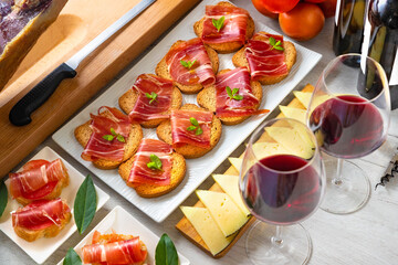 Spanish tapas and appetizers.Tapas and appetizers of Iberian ham with a glass of wine, ripe tomatoes and cow cheese on a white wooden background.