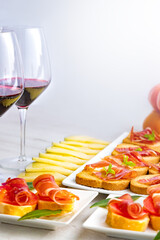 Spanish tapas and appetizers.Tapas and appetizers of Iberian ham with a glass of wine, ripe tomatoes and cow cheese on a white wooden background.
