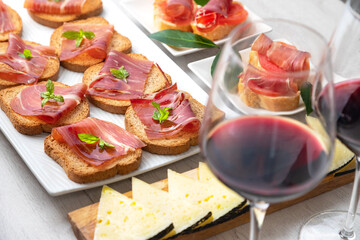 Spanish tapas and appetizers.Tapas and appetizers of Iberian ham with a glass of wine, ripe tomatoes and cow cheese on a white wooden background.