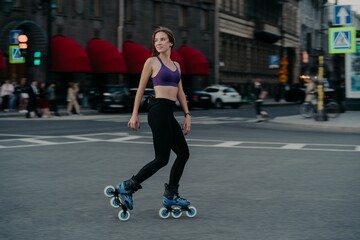Full length shot of active slim young woman dressed in sportsclothes rides on rollers to strengthen...