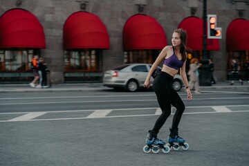 Fit woman involved in rollerskating wears top and leggings poses on busy road involved in popular...