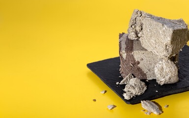 Piece of Halva on a slate board on yellow background with copy space. Traditional oriental dessert with cacao additions. Horizontal image. Side view.