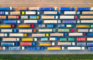 Aerial view of colorful trucks in terminal at sunset in summer. Top view of logistic center. Heavy industry. Transportation. Cargo transport, shipping. International trucking. View from drone of truck - obrazy, fototapety, plakaty