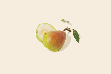 Sunlit, juicy, ripe green-red halved pear with green leaves, isolated on pastel beige background. Sun and shadow. Organic, raw natural healthy food concept. Minimal summer or autumn fruit arrangement.