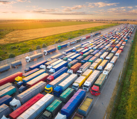 Aerial view of colorful trucks in terminal at sunset in summer. Top view of logistic center....