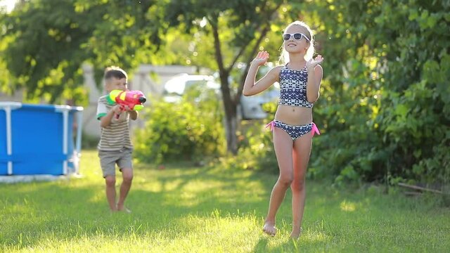 little boy is Splashing water on her older sister. Slow motion video of happy cheerful kids having fun in garden with water guns.