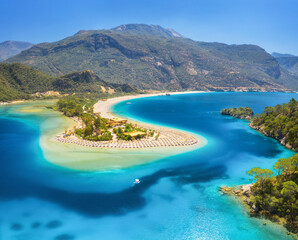 Aerial view of sea bay, sandy beach with umbrellas, trees, mountain at sunny day in summer. Blue lagoon in Oludeniz, Turkey. Tropical landscape with island, white sandy bank, blue water. Top view