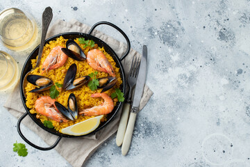 Traditional spanish seafood paella in pan with chickpeas, shrimps, mussels, squid on light grey concrete background. Top view with copy space