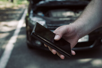 hand holds a mobile phone on the background of the car. Calls a tow truck help