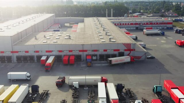 Aerial side view of the logistics park with loading hub. A lot of semi-trailer trucks standing at warehouse ramps for loading and unloading goods