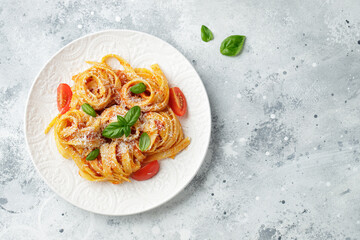 Tasty appetizing classic italian tagliatelle pasta with tomato sauce, cheese parmesan and basil on plate on light table. View from above, horizontal. Top view with copy space