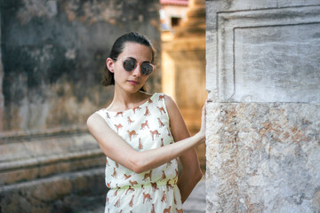 fashionable cute girl in a yellow dress and sunglasses standing and looking at the camera