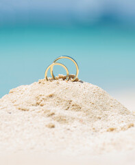 Pair wedding rings in sand on tropical beach