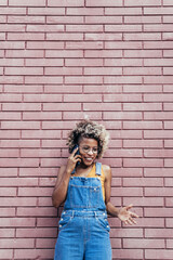 Cool black African American Woman with blond hair on a phone call over a brick wall