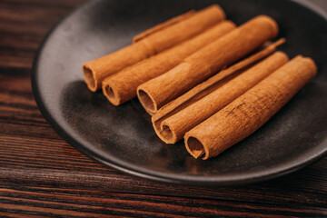 brown cinnamon sticks lie on a black plate, wooden background