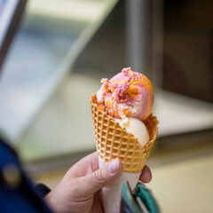 Fruit ice cream mix in waffle cone in female hand. Selective focus. Real scene