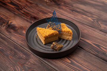 honey cake decorated with decor on a black beautiful plate, wooden background