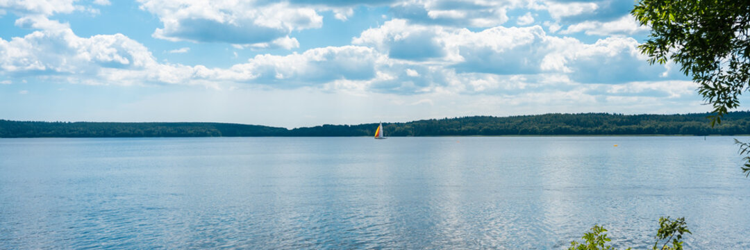 Panorama view of the Baltic Sea Bay on sunny summer day. Rocky shores of Scandinavia covered with evergreen forest. Beautiful white sailing yacht floating along coast of Sweden. Blue sky white clouds.