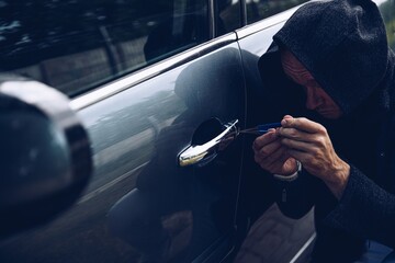 Car thief breaking into car with picklock or screwdriver.