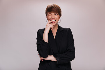 Charming girl in black jacket winking on isolated background. Short-haired woman in dark outfit...