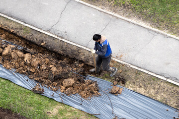Migrant labor. A worker digging a ditch along a pavement in summer.