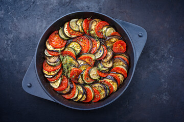 Modern style traditional French ratatouille with tomatoes, eggplant and zucchini served as top view in a rustic cast-iron skillet with copy space - obrazy, fototapety, plakaty