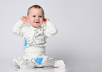 cute blue-eyed baby in a white sandpit bodysuit with a kitten print, sits on the floor and touches...