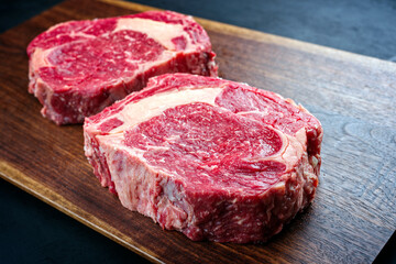 Modern style raw dry aged wagyu rib-eye beef steaks offered as close-up on a wooden design board with copy space