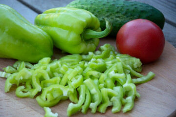 Red tomato, cucumber and bell peppers in strips lie on a wooden background. Harvest fresh vegetables from the garden.