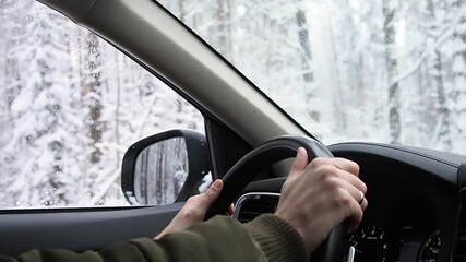 Car driving on snow covered road through winter snowy forest. View from side mirror with man hands