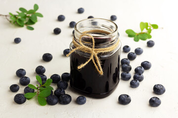 Bluberry jam in a glass jar and fresh blueberries on a light background