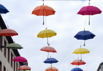 Vor blauem Himmel in Reihen hängende, bunte Regenschirme