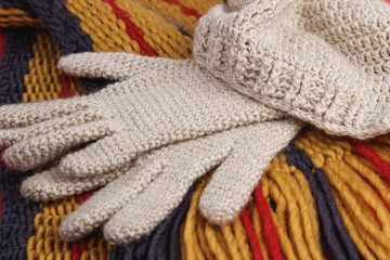 Fototapeta na wymiar Close up shot of crocheted wool hat and gloves, natural white, over yellow, violet and red scarf. Warm clothing