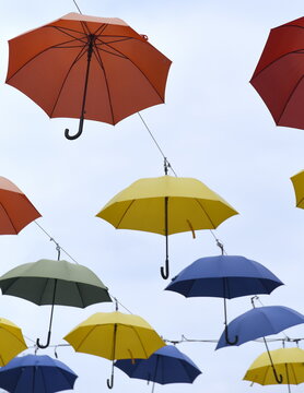 Vor blauem Himmel in Reihen hängende, bunte Regenschirme