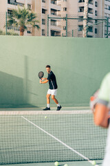 Fototapeta na wymiar Man training paddle tennis on an outdoor green paddle tennis court behind the net with his coach