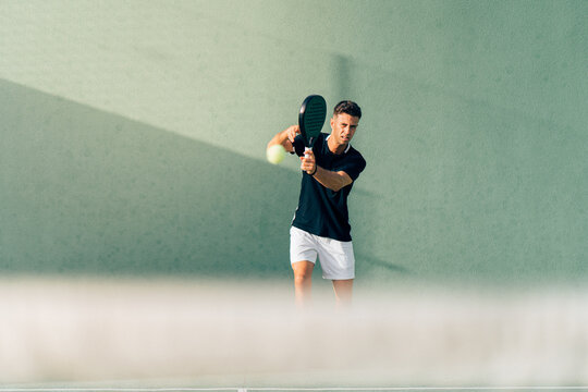Man playing paddle tennis on an outdoor green paddle tennis court at the sunset