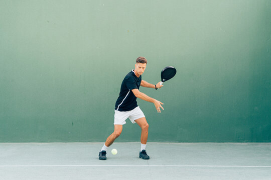 Man playing paddle tennis on an outdoor green paddle tennis court at the sunset