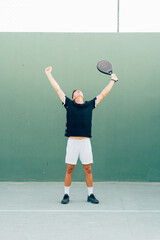 Paddle tennis player celebrating victory at the end of the match on the green court at sunset