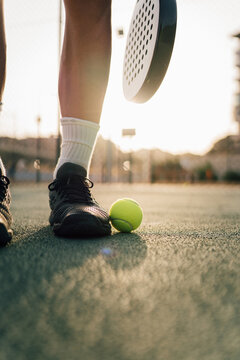 Man lifting paddle ball with his racket and shoe on the green court during training in the sunset